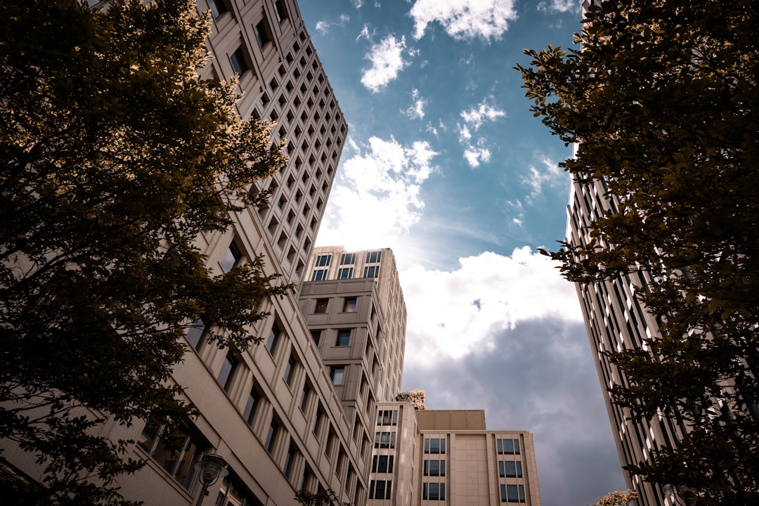 From a low angle, a single person stands on a city street looking up at the imposing facade of a massive, modern glass skyscraper, symbolizing a solo agent's challenge.
