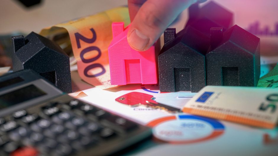 A professional desk with a miniature house model next to a calculator, illustrating the financial planning involved in real estate commissions.